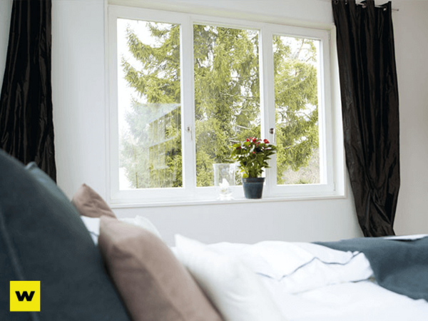 Helles Schlafzimmer mit großem Fenster, Zimmerpflanze, Bett und Blick ins Grüne.